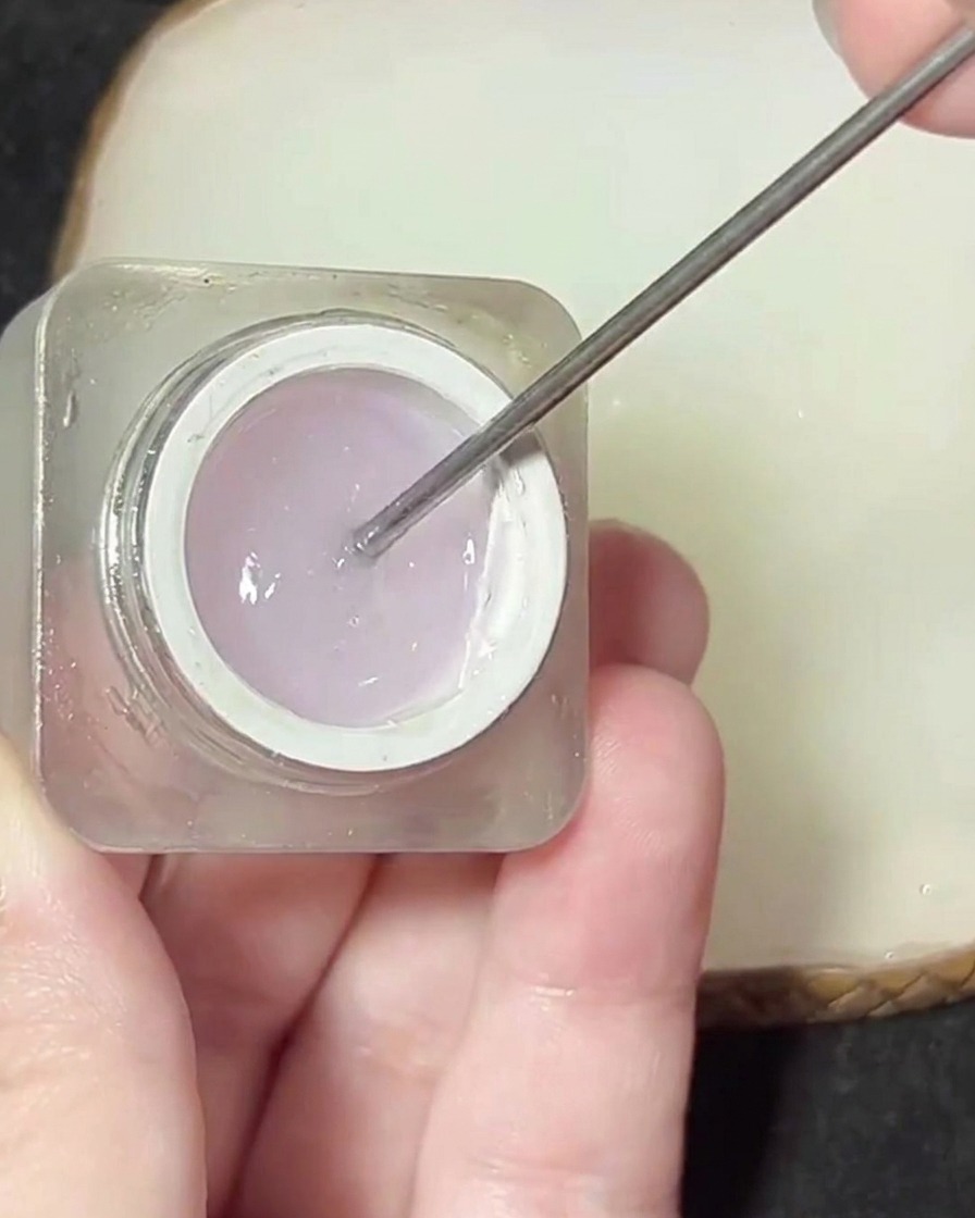 Ein Metallspatel hebt ein klares, dickflüssiges Gelprodukt aus einem kleinen Tiegel.