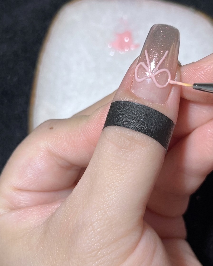 Nahaufnahme eines feinen Pinsels, der eine kleine weiße Perle in der Mitte einer 3D-Gelschleife auf einem Chrome-Nagel platziert.