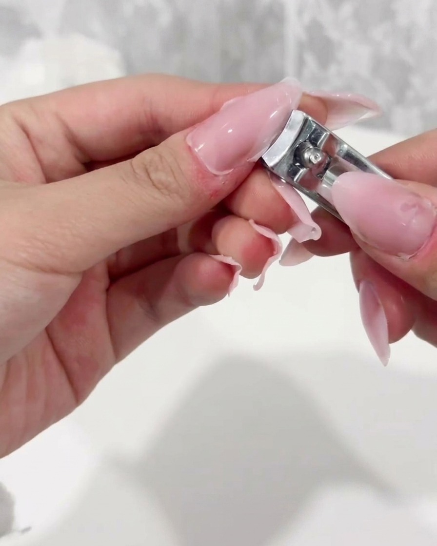 Ein Nagelknipser kürzt die freie Kante eines klaren Kunststoff-Nagel-Tips.