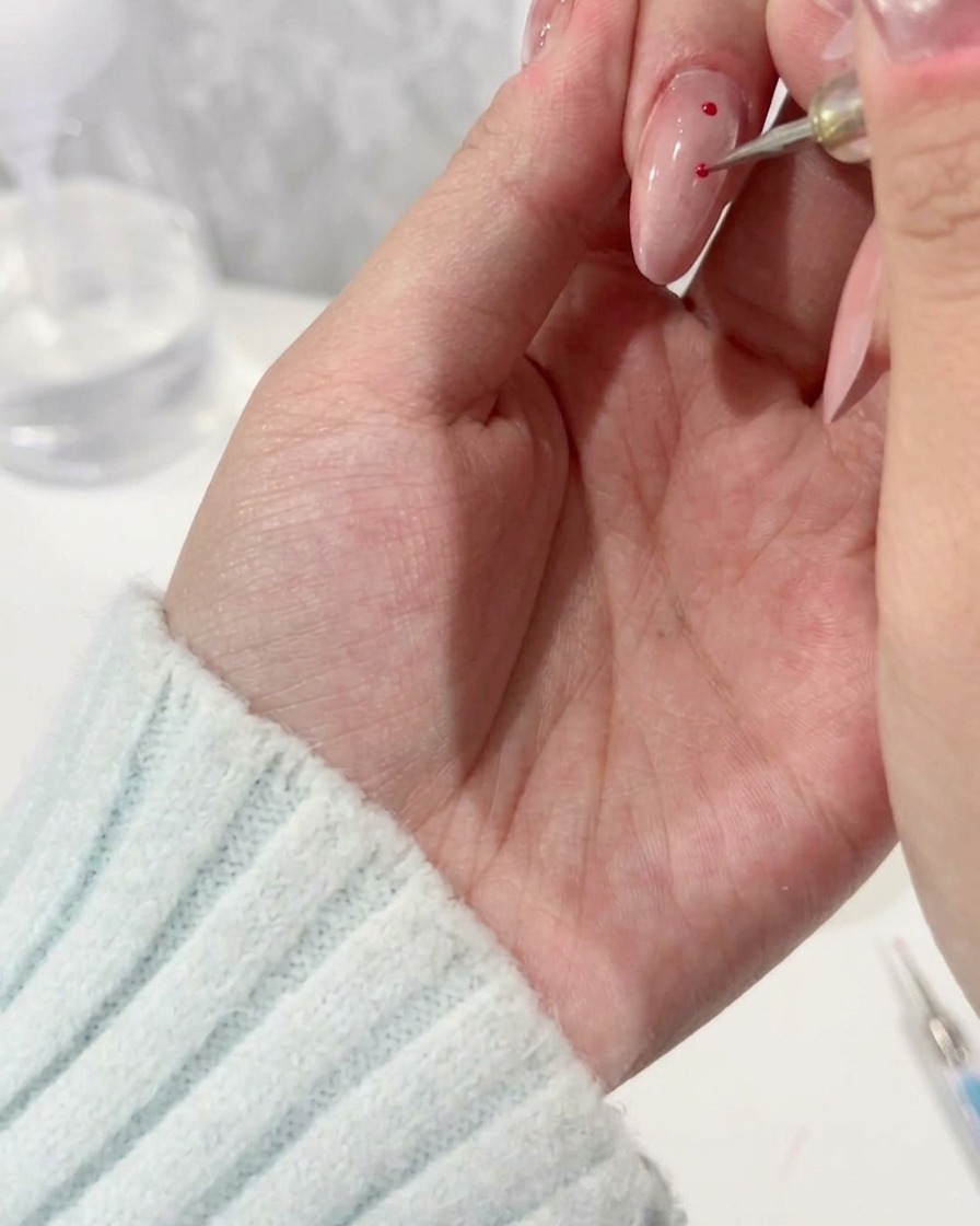 Ein Dotting-Tool setzt präzise magentafarbene Punkte auf die helle Nagelbasis.