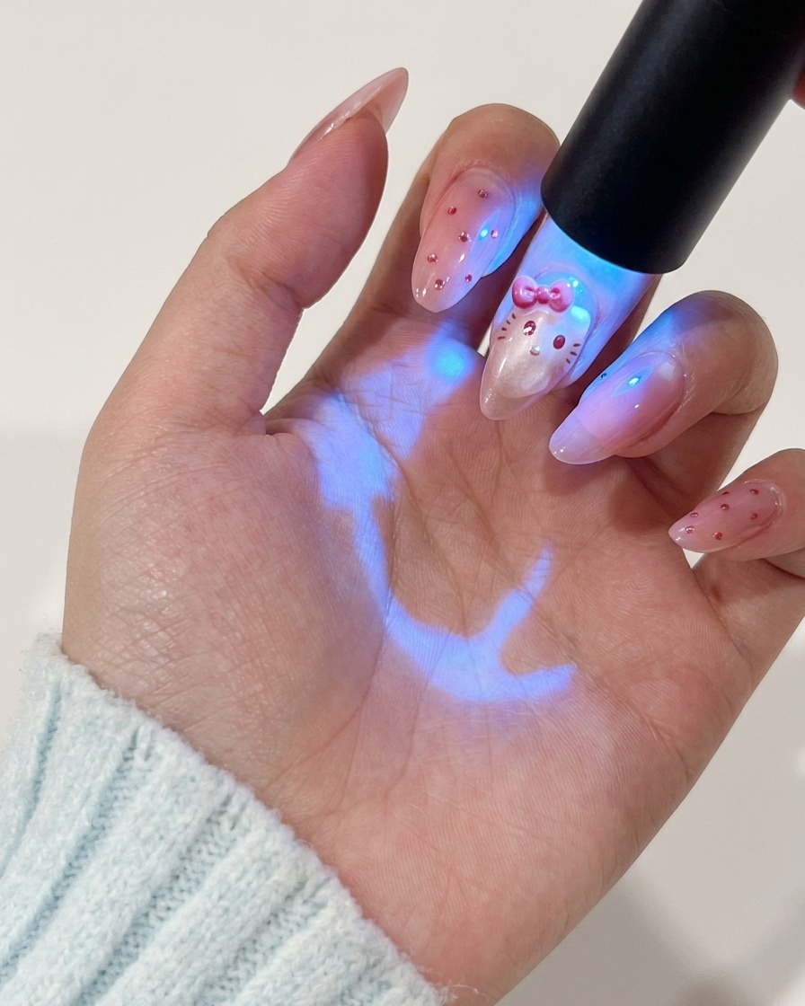 Eine Hand hält eine UV-Lampe über den Fingernagel, um das aufgemalte Charakter-Design auszuhärten.