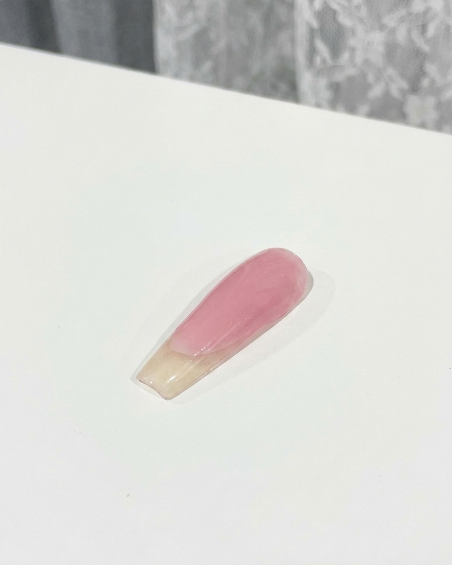 Ein Pinsel trägt eine Schicht Top Coat über einen 3D-rosa Schleifen-Charm auf, der auf einem Nagel befestigt ist.