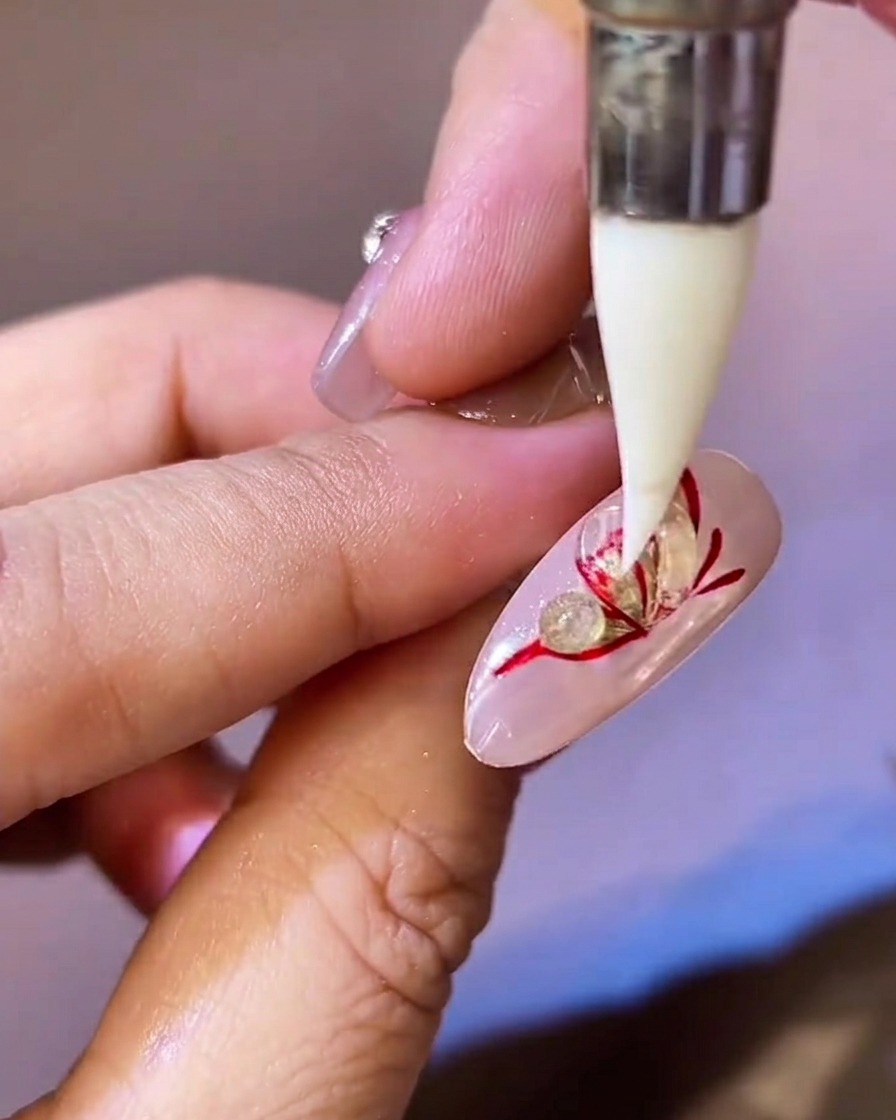 Ein spitzes Silikonwerkzeug drückt ein Kügelchen aus klarem Gel auf dem Nagel flach.