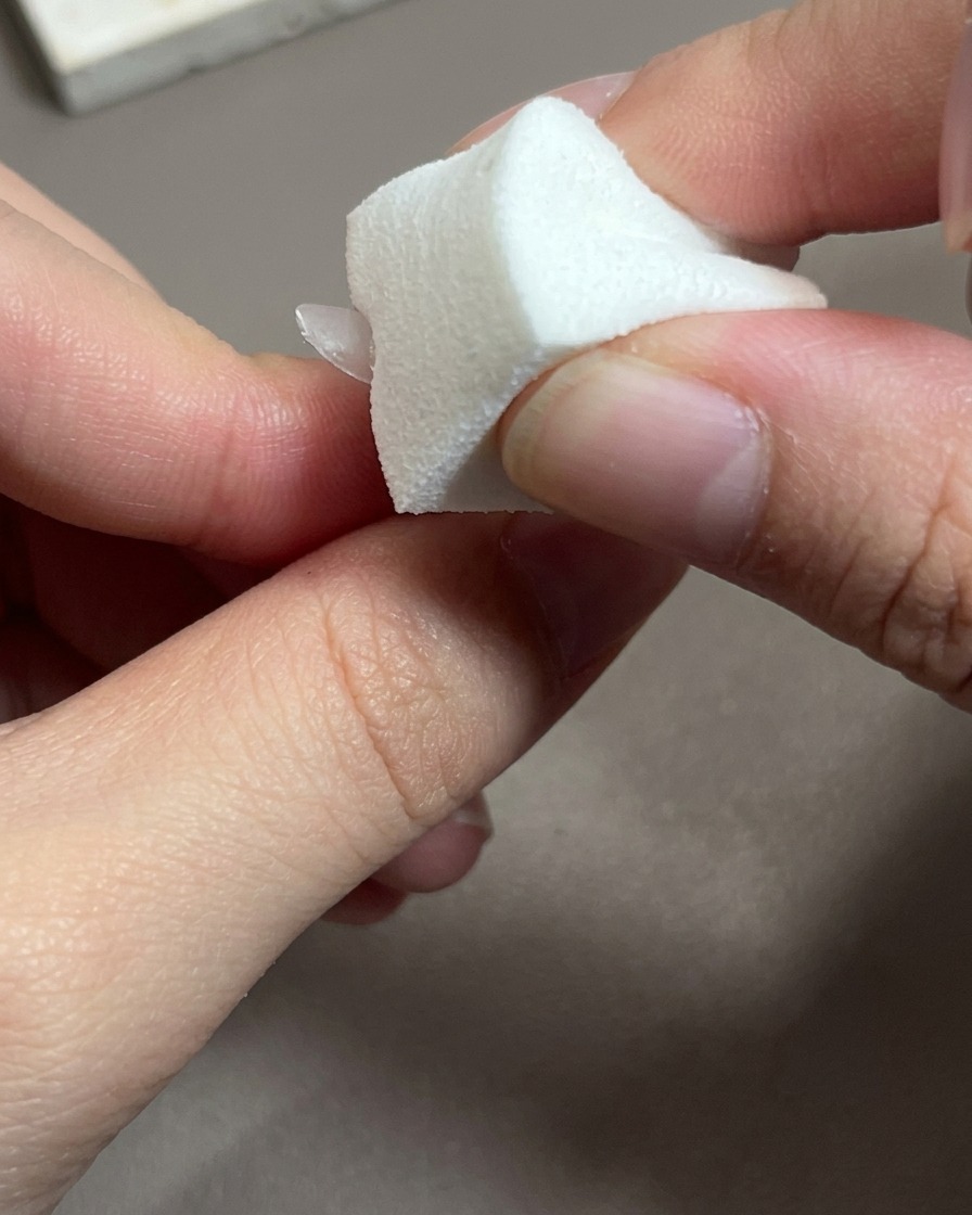 Nahaufnahme eines Pinsels, der einen transparenten, rosafarbenen Base Coat auf einen Nageltip aufträgt.