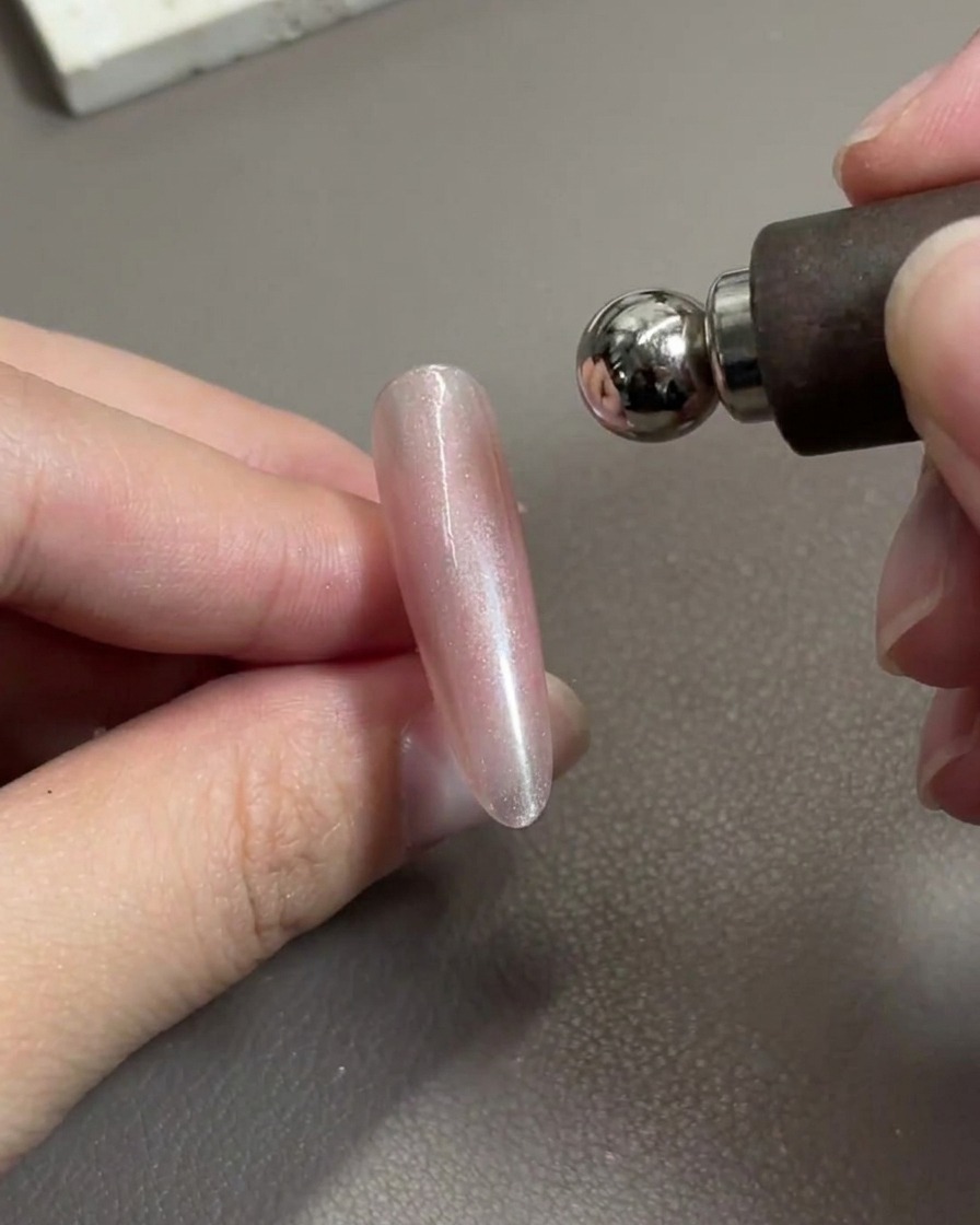 Ein Magnetwerkzeug wird über einen glänzenden rosa Gelnagel gehalten und verschiebt aktiv die metallischen Partikel.
