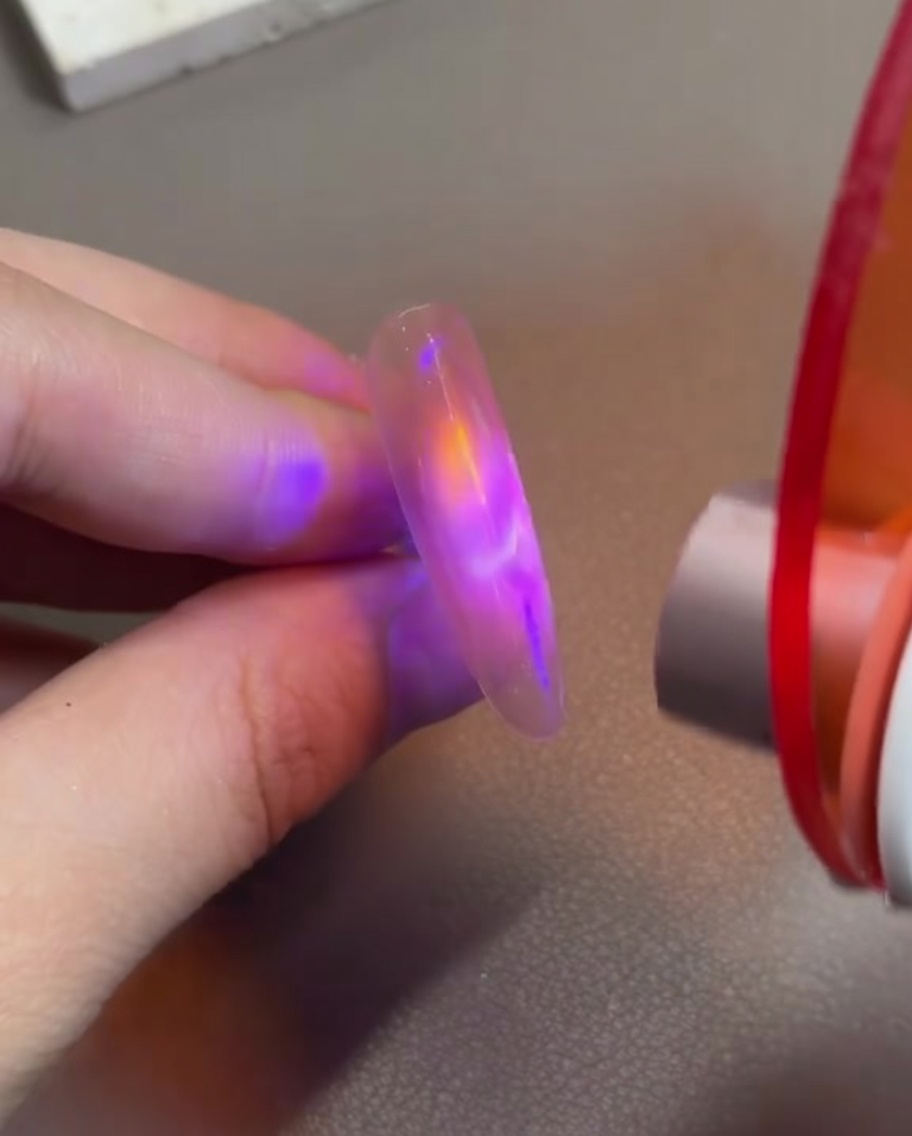 Ein Finger mit rosafarbenem Cat-Eye-Gel wird unter eine kleine, handgehaltene LED-Härtungslampe gehalten, um das Magnetdesign zu fixieren.