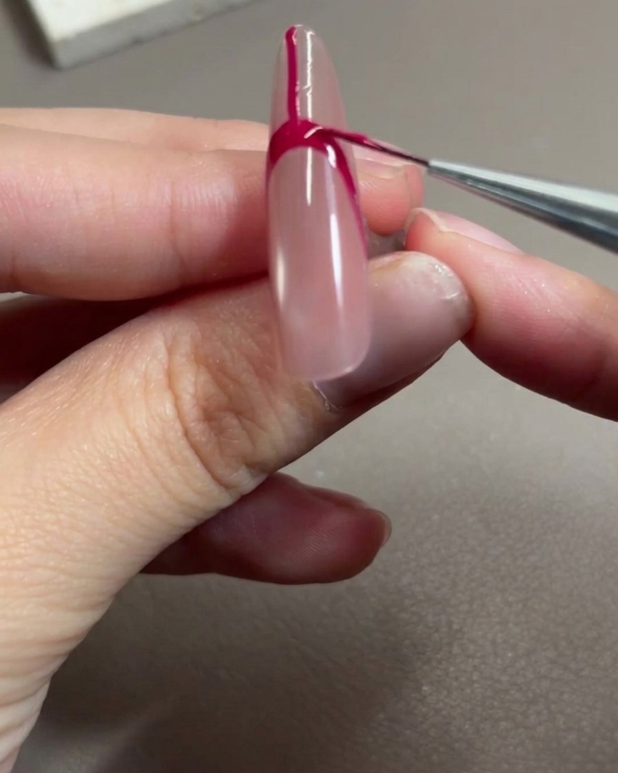 Ein Nailart-Pinsel trägt rosenrotes Gel auf, um den Raum innerhalb der French-Tip-Kontur zu füllen.