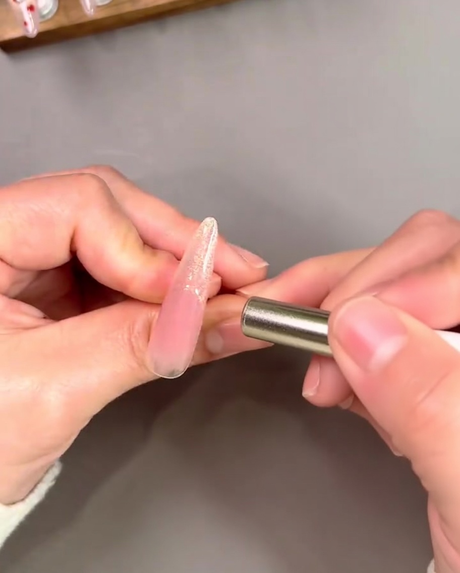 Ein Magnet wird nahe an eine goldene French-Spitze gehalten, um einen konzentrierten, reflektierenden Cat-Eye-Effekt zu erzielen.