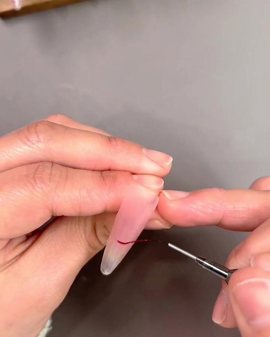 Detailansicht eines Liner-Pinsels, der eine French-Spitze mit einer feinen roten Gel-Linie umrandet.