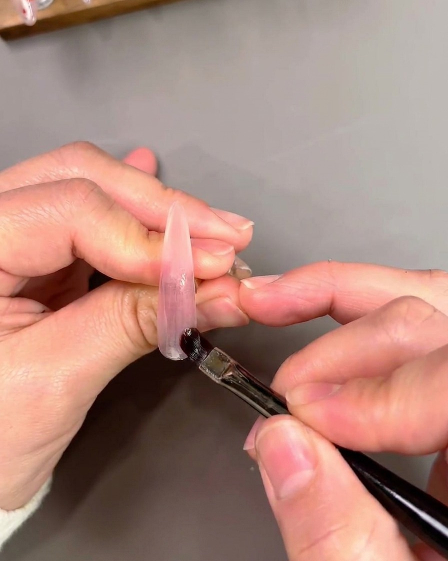 Ein flacher Gel-Pinsel trägt violettes Cat-Eye-Gel auf und verblendet es auf einem künstlichen Nagel.