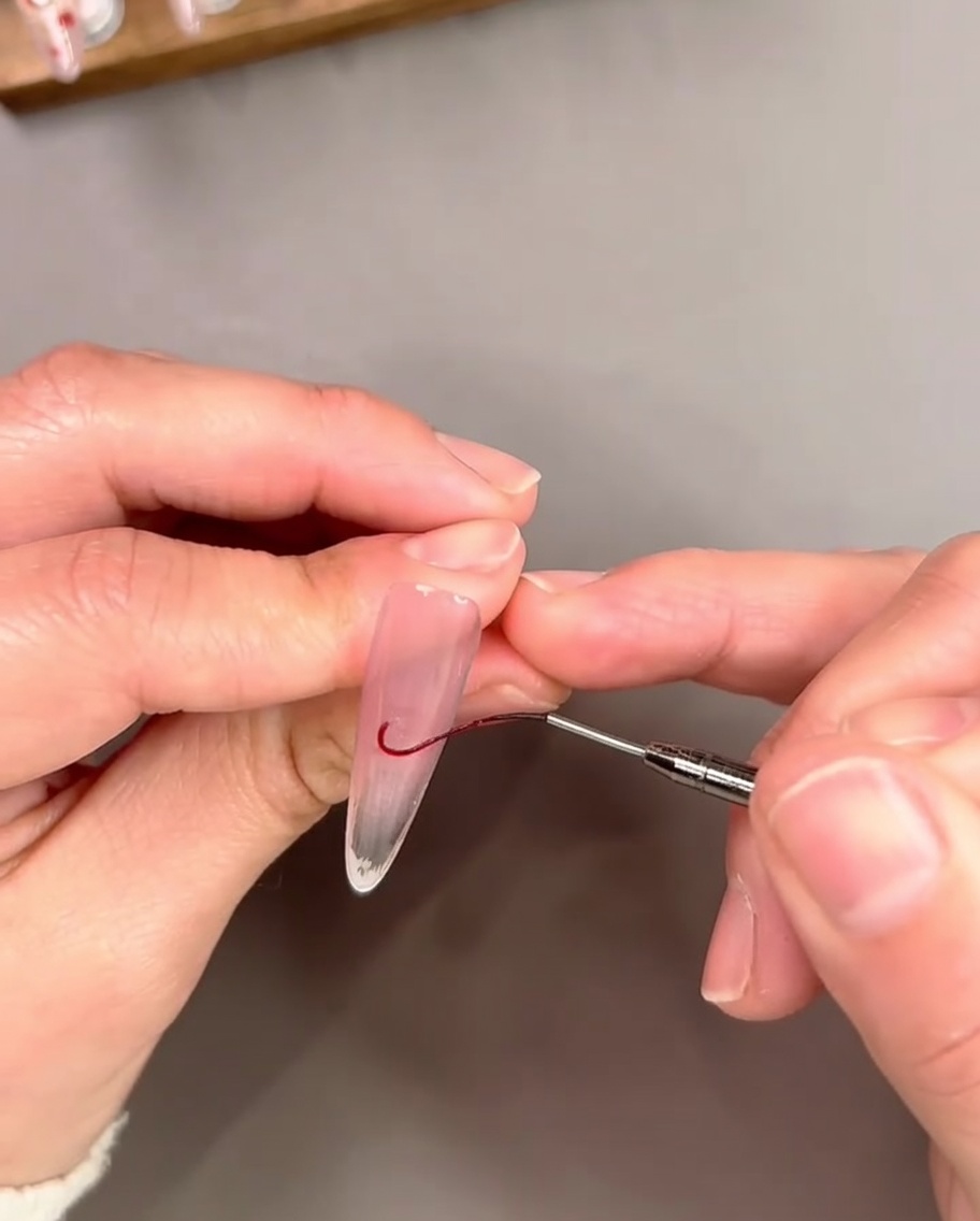 Ein feiner Liner-Pinsel zeichnet eine dünne, geschwungene rote Gel-Linie nahe der freien Nagelspitze, um eine French-Spitze zu umranden.