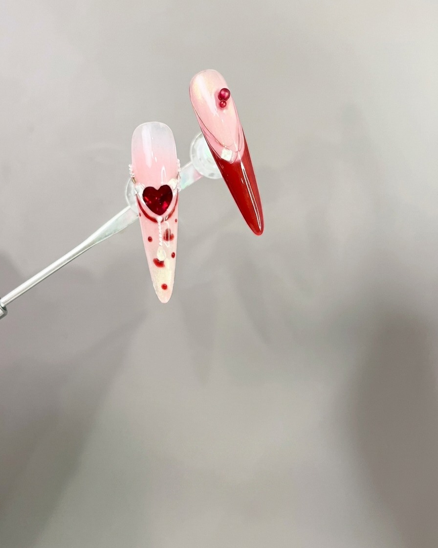 Eine Pinzette platziert einen roten 3D-Schleifen-Charm auf einer manikürten Nagelspitze.