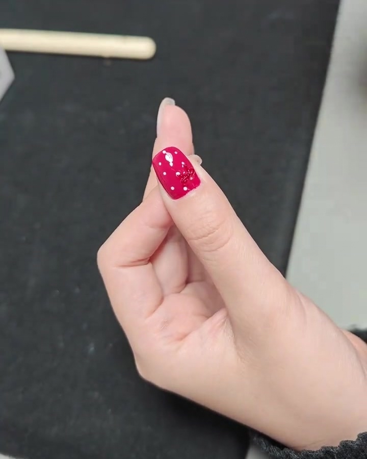 Eine Nahaufnahme einer Hand mit einem fertigen roten Nagel mit Polka-Dots und Schleife in einer professionellen UV-Nagellampe.