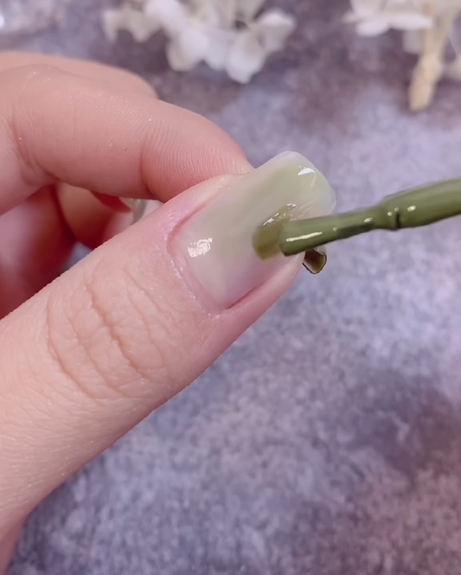 Ein Pinsel verblendet grünes Gel auf einer Nageloberfläche, um einen Gradienten-Effekt zu erzeugen.