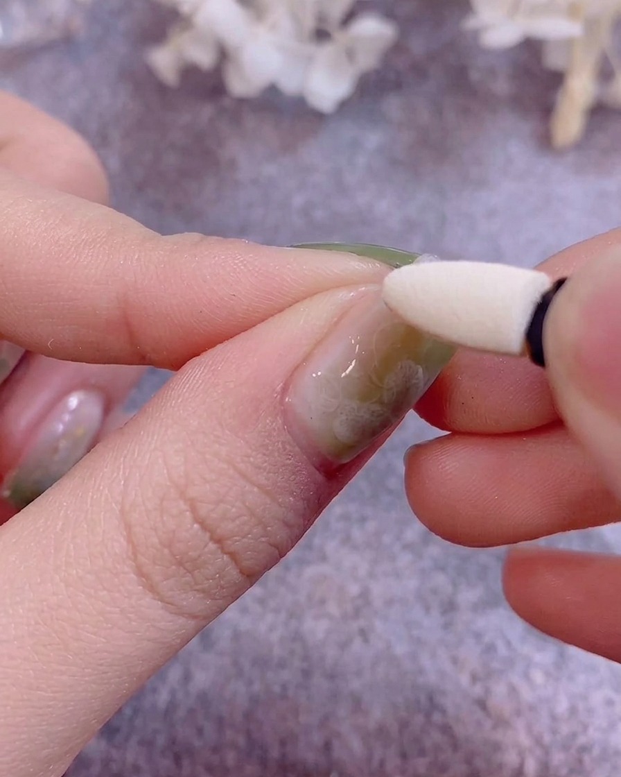 Ein Silikon-Applikator poliert metallisches Chrom-Puder auf einen mit Gel lackierten Nagel.