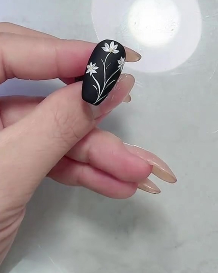 Makroaufnahme des fertigen Gänseblümchen- und Blattdesigns auf einem mattschwarzen Nagel mit Fokus auf die Kanten.