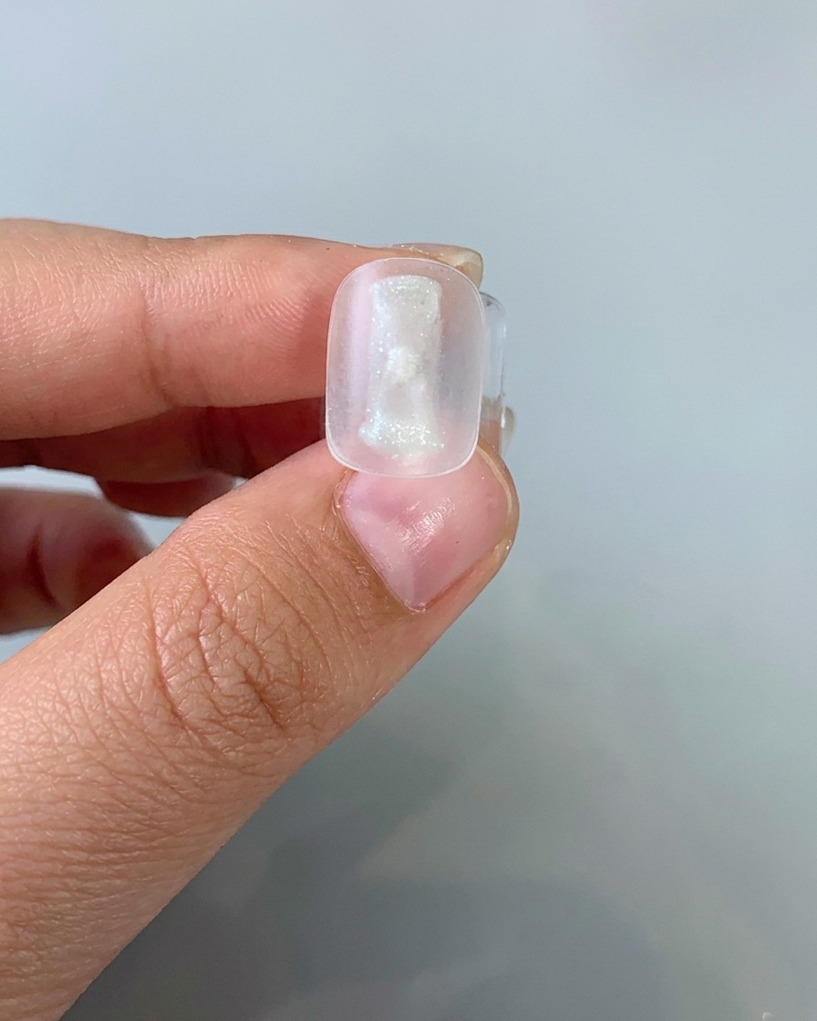 Ein Pinsel trägt eine dünne Schicht helles Cat-Eye-Gel auf einen Nagel-Tip auf.
