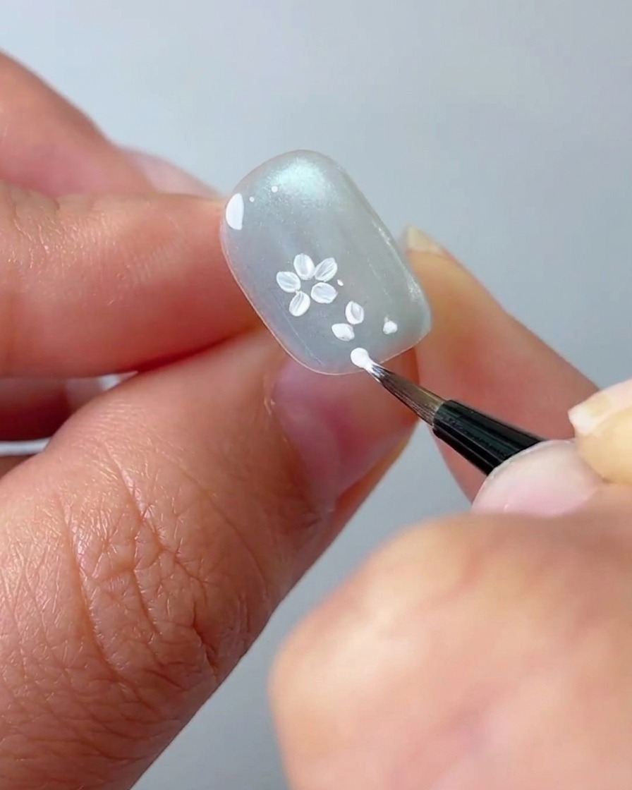 Ein Liner-Pinsel fügt einem Blumen-Cluster auf dem Nagel weitere Details weißer Blütenblätter hinzu.