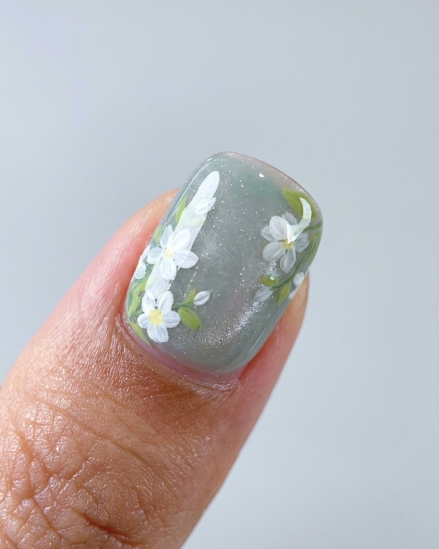 Eine Nahaufnahme eines Pinsels, der weiße Details auf Gänseblümchen-Blütenblätter auf einem Nagel hinzufügt.