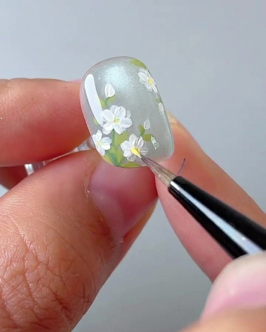 Eine Nahaufnahme eines Nageldesigners, der einen gelben Punkt in die Mitte eines weißen Gänseblümchens setzt.