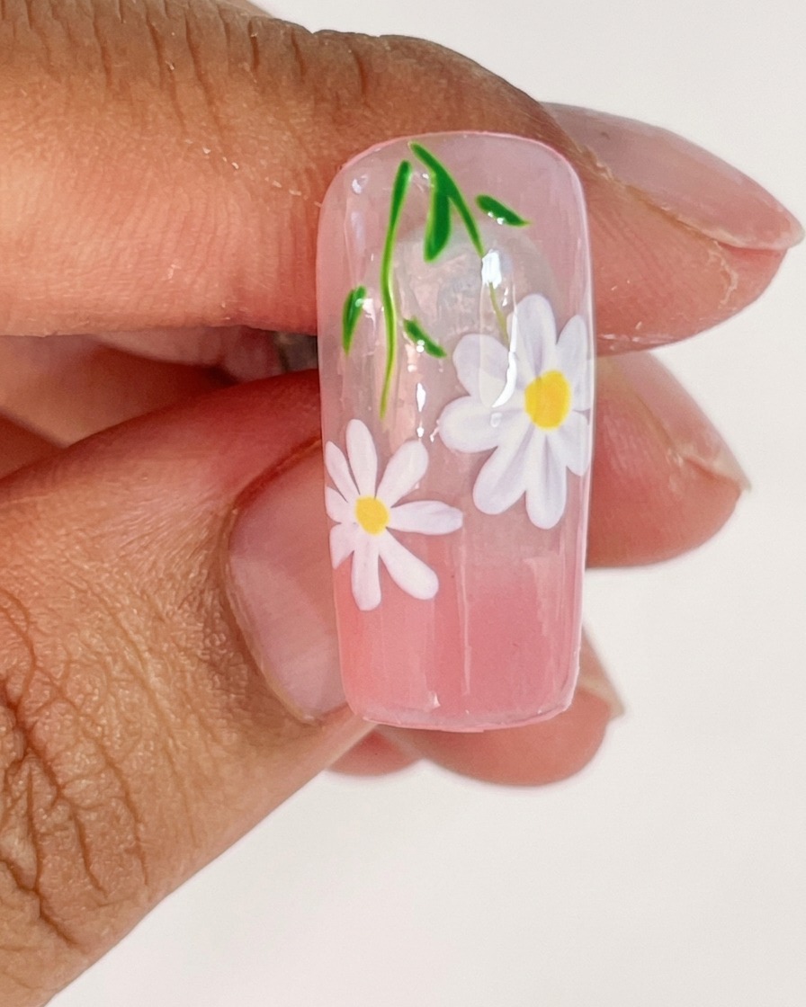 Ein Nageltipp wird in einer UV-Lampe platziert, um die frisch gemalten weißen Blütenblätter auszuhärten.
