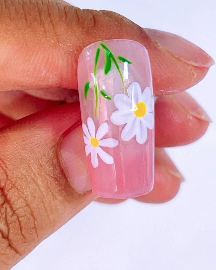 Nahaufnahme eines rosafarbenen Ombré-Nagels, der mit einem zweiten, kleineren Gänseblümchen bemalt wird.