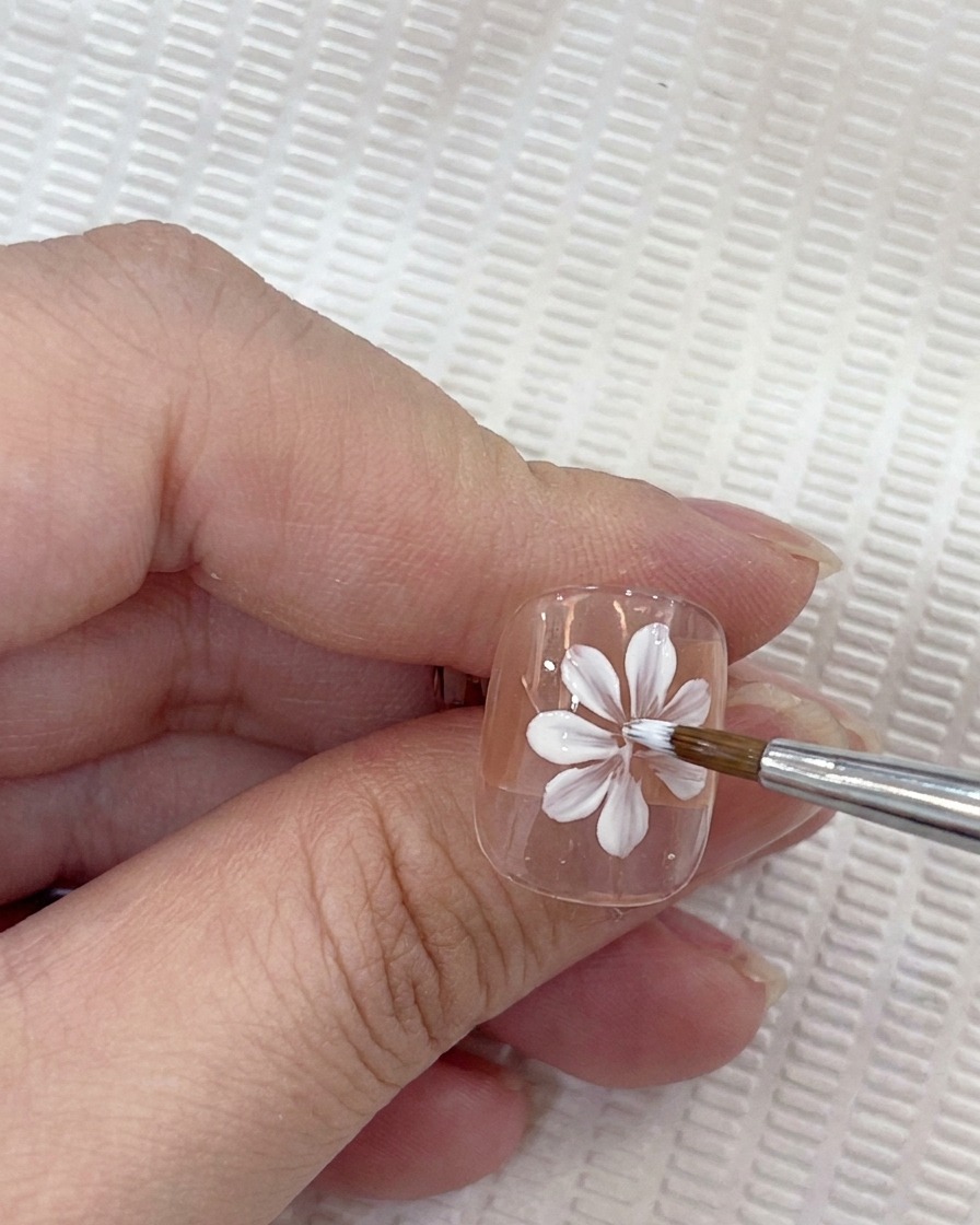 Drei weiße Blütenblätter auf dem Nagel, die ein Dreiviertelkreuz bilden.