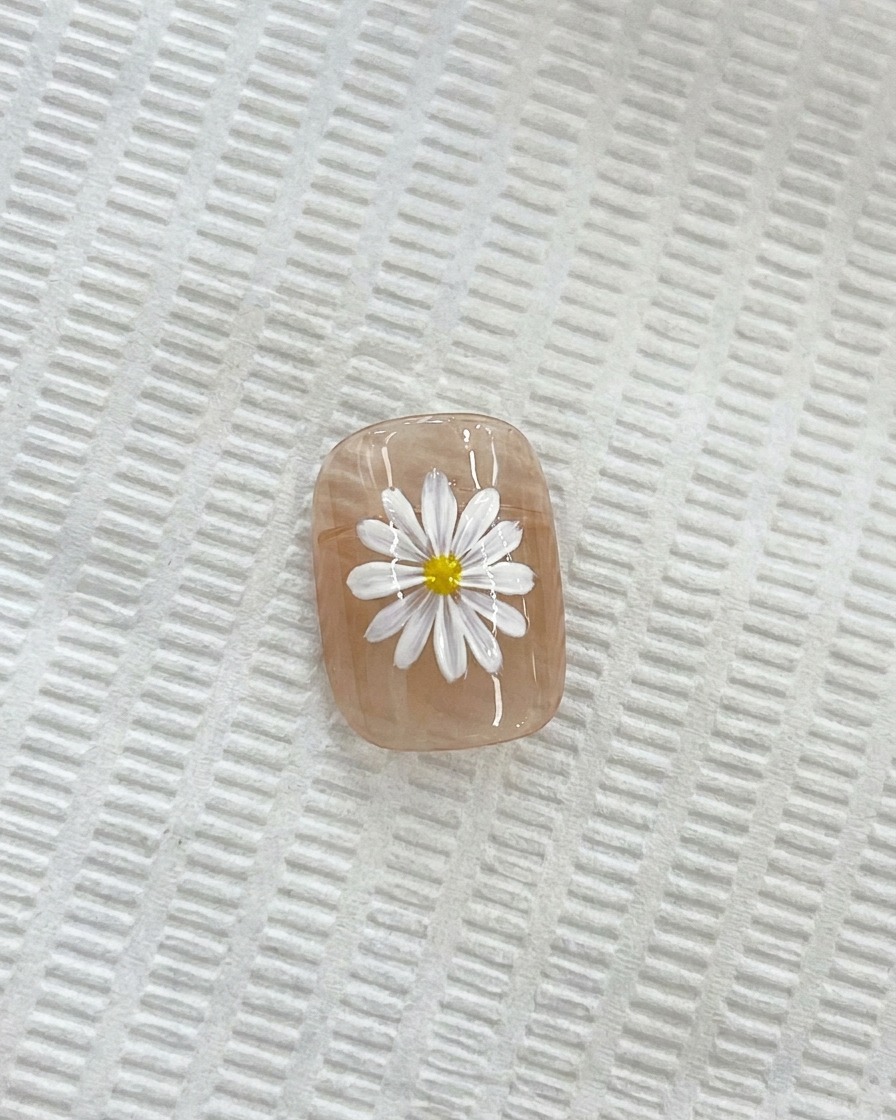 Nahaufnahme eines weißen Gänseblümchens auf einem Nagel, bei dem ein Detailpinsel eine gelbe Mitte aufträgt.