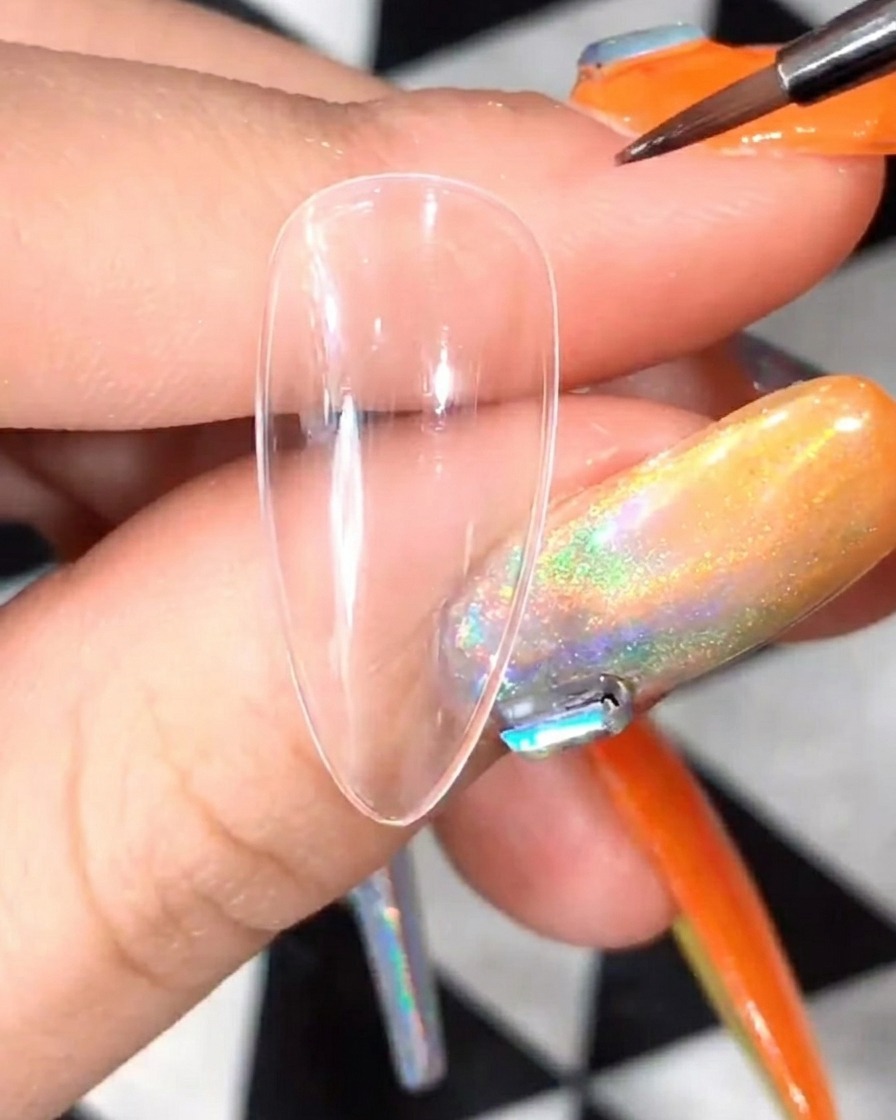 Nahaufnahme eines Detailpinsels, der weißes Gel aufträgt, um die ersten Blütenblattformen für ein Gänseblümchendesign auf einem klaren Nagel-Tip zu formen.