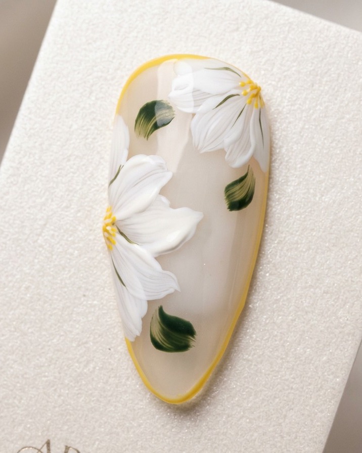 Eine Nahaufnahme eines Nagel-Tips zeigt, wie ein weißer Punkt in die Mitte eines gelben Blumenkerns gesetzt wird.
