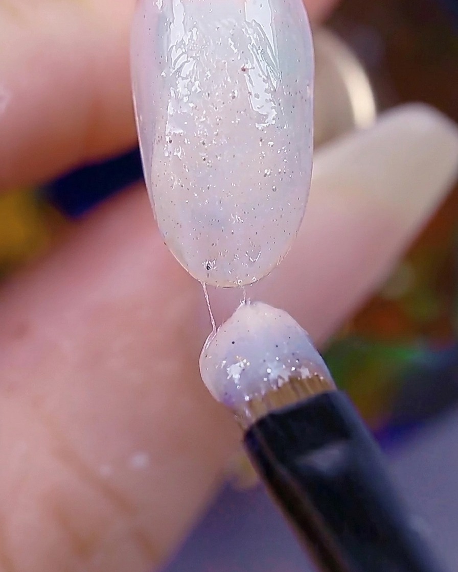 Ein Nagelpinsel trägt eine zweite Schicht Sugar-Gel auf, wobei die Nageloberfläche texturiert und bereit für die Aushärtung erscheint.