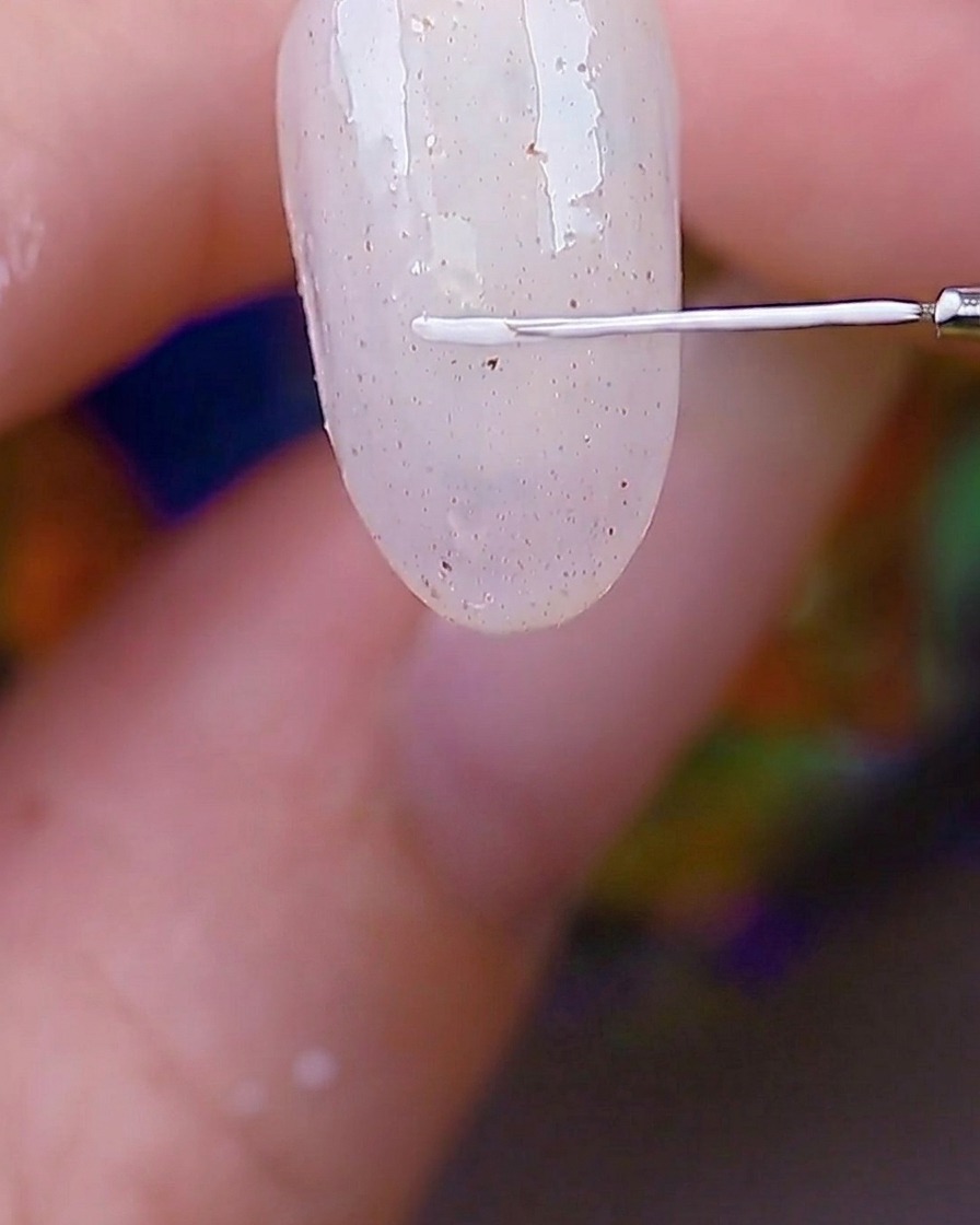 Detailaufnahme eines feinen Liner-Pinsels, der einen weißen rechteckigen Rahmen in die Ecke eines texturierten Nagels zeichnet.