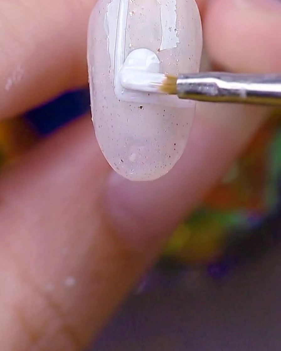 Ein kleiner Rundpinsel füllt das weiß umrandete Rechteck auf dem Nagel mit deckendem weißen Gel.