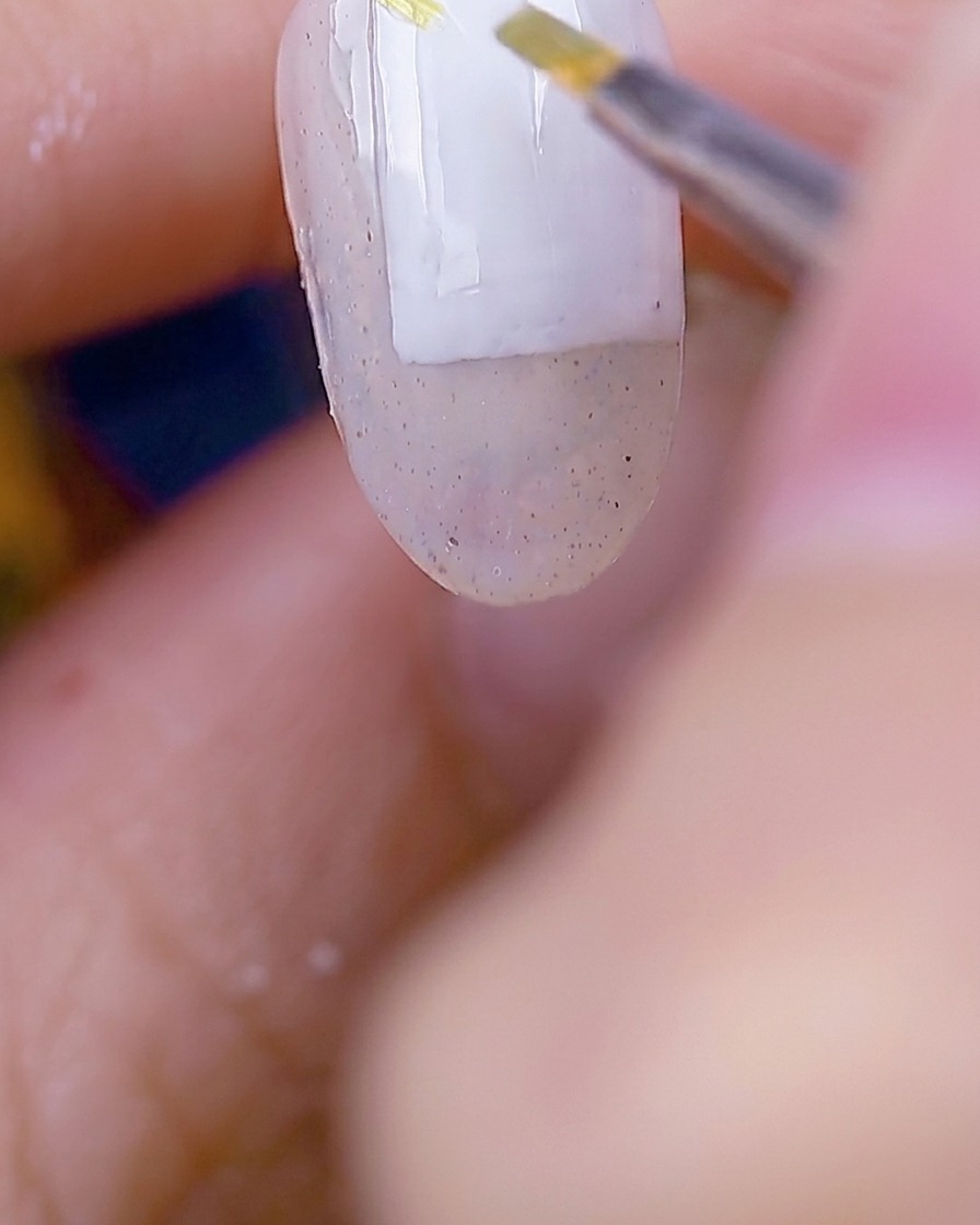 Ein Pinsel trägt moosgrünes Gel auf, um zarte Blattformen über der vorbereiteten Nageloberfläche zu erzeugen.