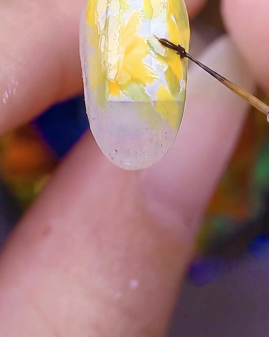Nahaufnahme eines Nagels, der gelbe Blütenblätter zeigt, bei dem ein feiner Pinsel winzige braune Punkte genau in die Mitte setzt.