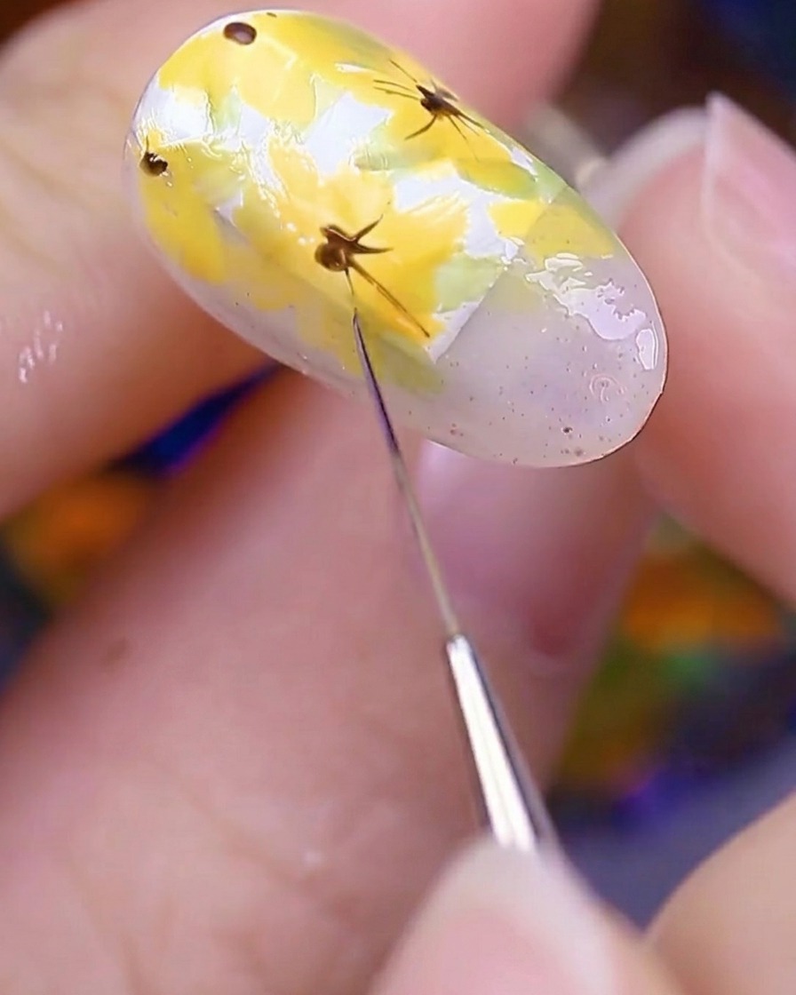 Nahaufnahme des bemalten Nagels, der unter einer UV-Nagellampe gehalten wird, um die frisch aufgetragenen floralen Details auszuhärten.
