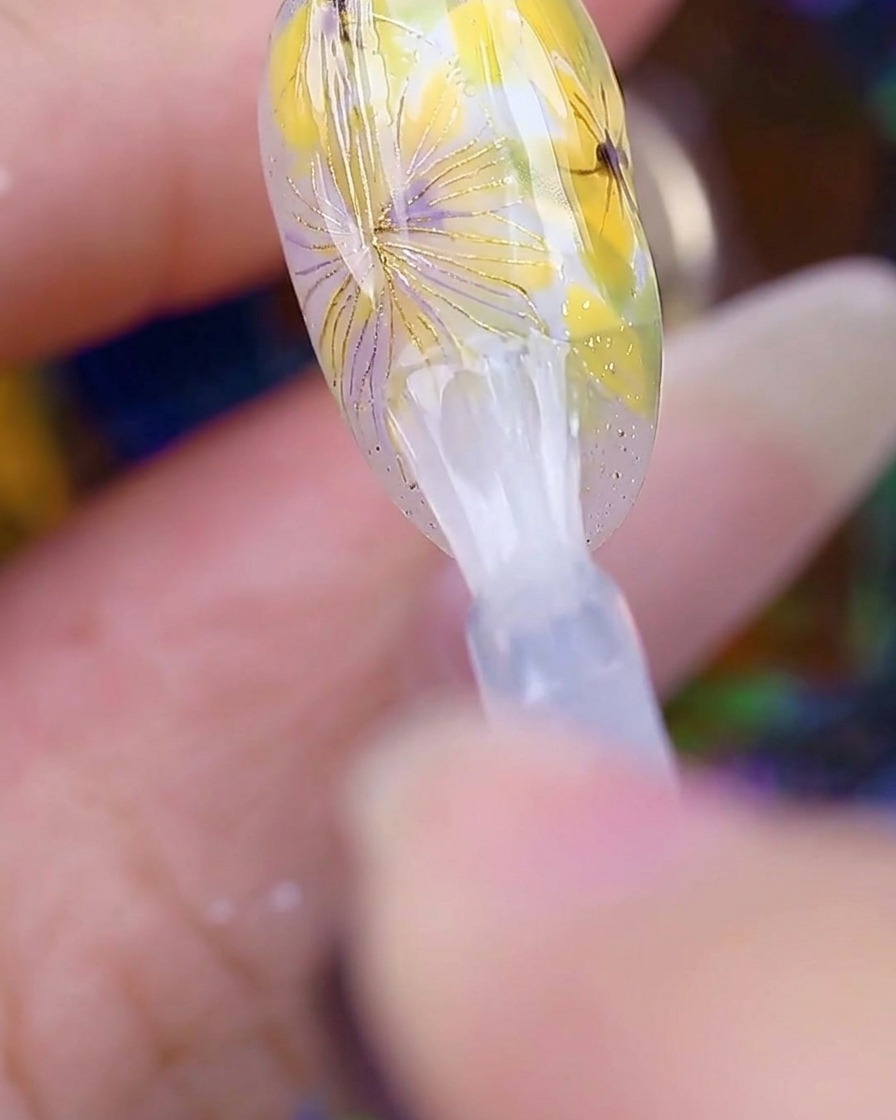 Ein Pinsel trägt einen klaren, glänzenden Top Coat über die fertige Gänseblümchen-Nailart auf, wodurch die Oberfläche glatt und glänzend aussieht.