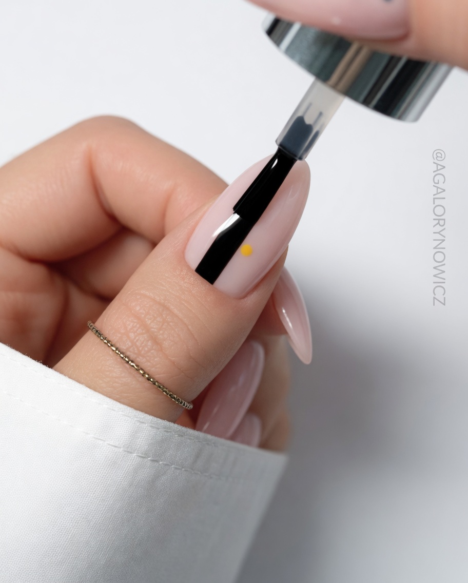 Detailaufnahme, wie ein drittes weißes Blütenblatt auf den Nagel gemalt wird.