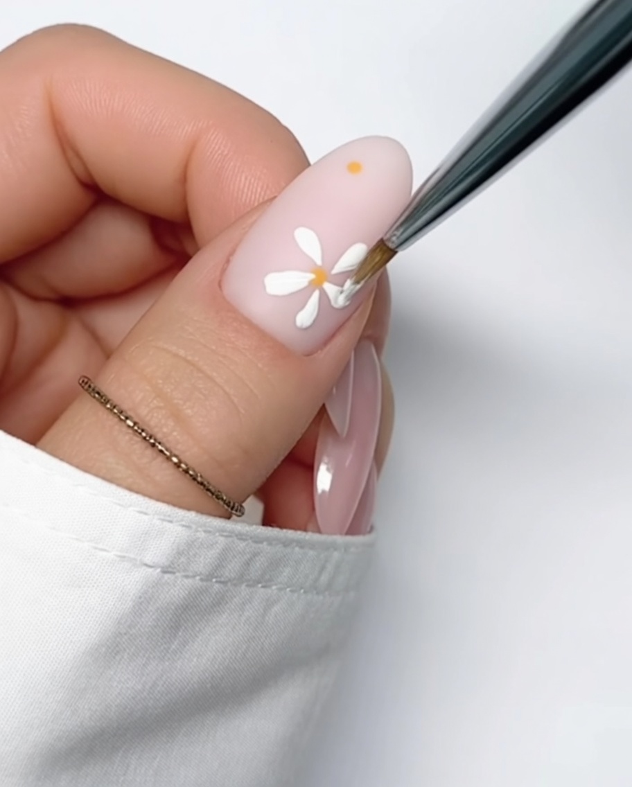 Nahaufnahme eines nudefarbenen Nagels mit einem kleinen, präzisen gelben Gelpunkt als Vorbereitung für ein weiteres Gänseblümchen.