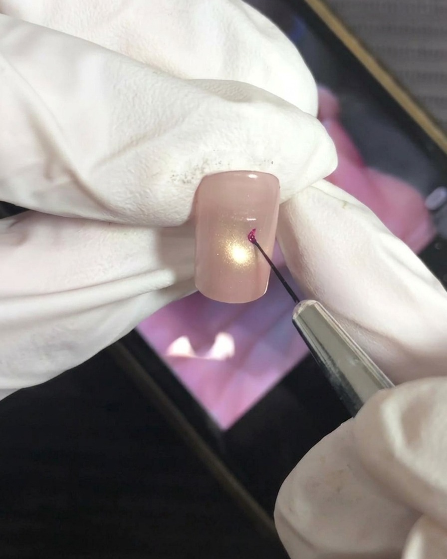 Ein feiner Liner-Pinsel trägt vorsichtig einen Punkt magentafarbenes Gel auf die Mitte des Nagels auf.