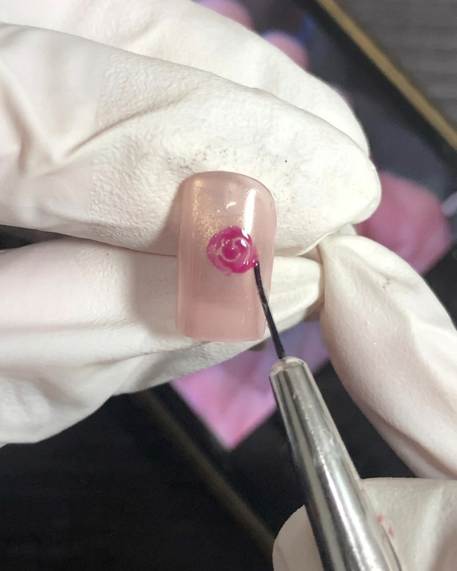 Nahaufnahme eines Nailart-Pinsels, der die äußeren Ränder eines Rosen-Designs auf einer Nude-Basis verblendet.