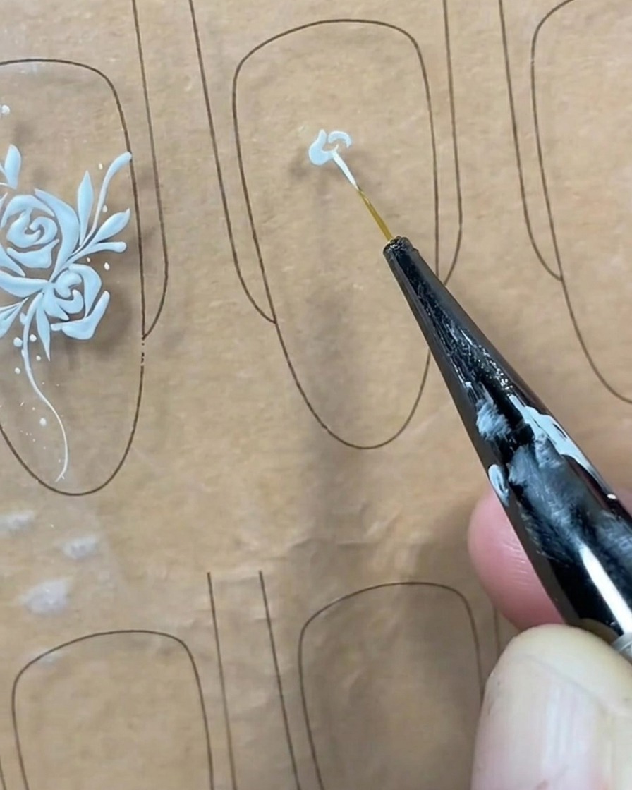 Nahaufnahme eines Liner-Pinsels, der einen kleinen Punkt weißes Gel in die Mitte eines transparenten Nageltips setzt.