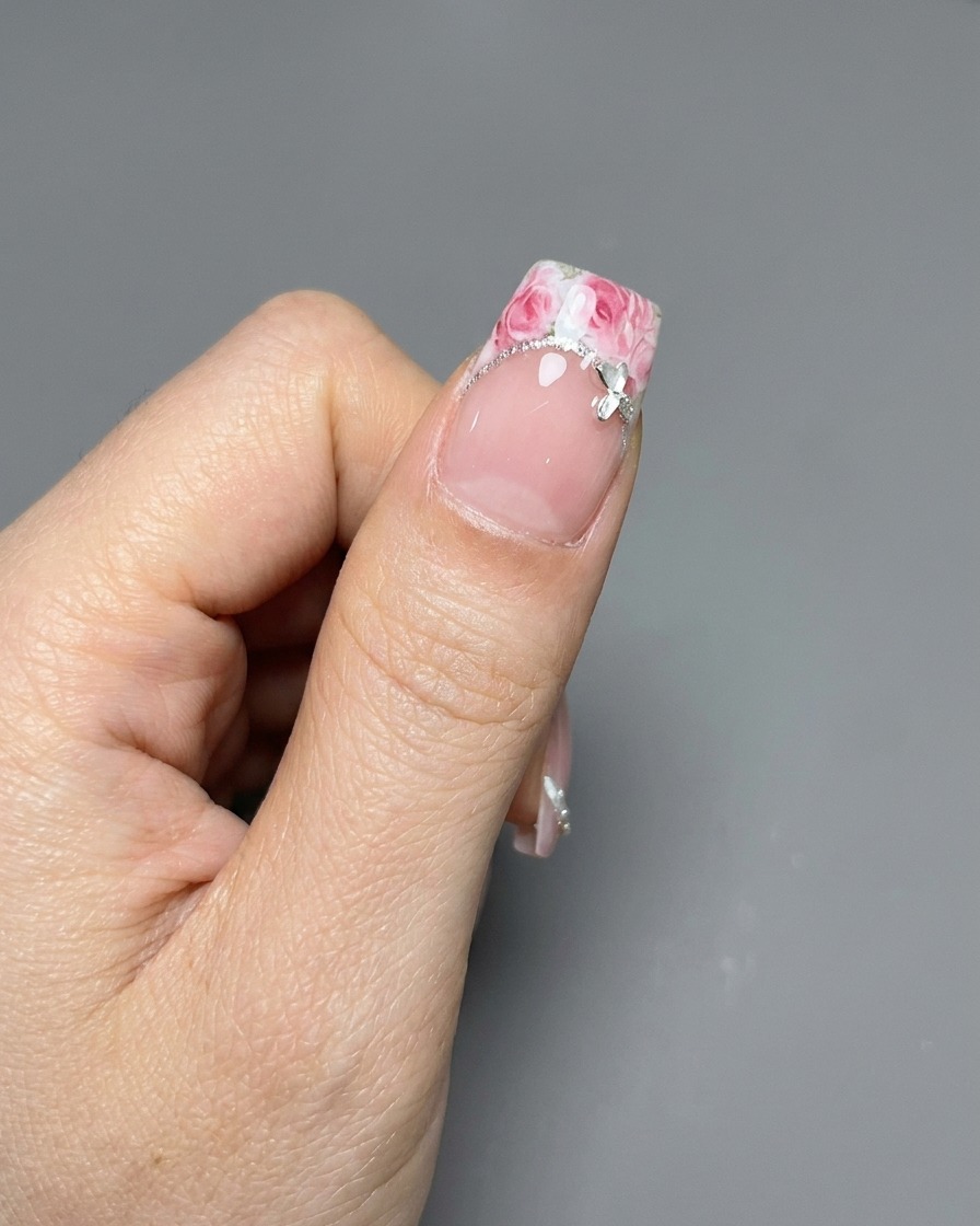 Eine Pinzette platziert einen Rosen-Aufkleber auf einer French-Spitze.