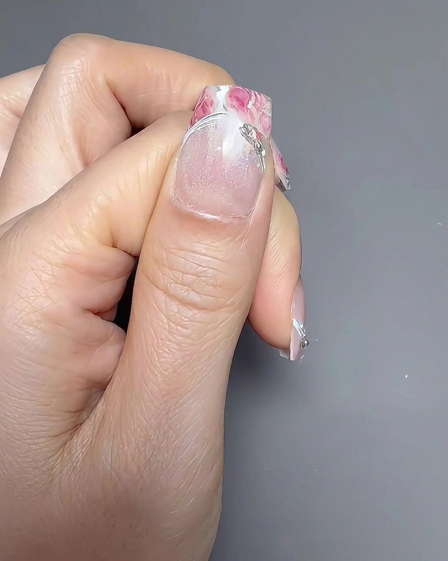 Ein Nagellackpinsel trägt einen klaren, glänzenden Top-Coat auf den blumig verzierten Nagel auf.