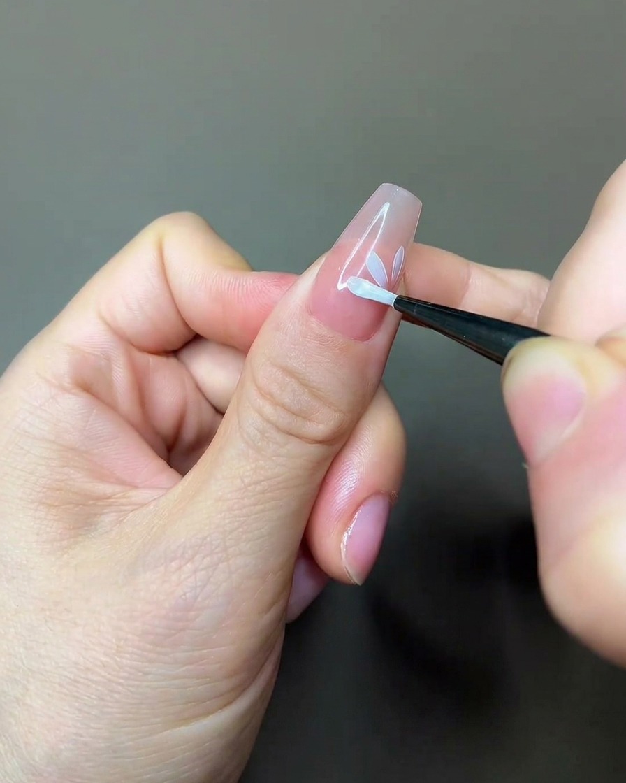 Ein Nagelpinsel trägt eine Schicht matten Überlack über ein teilweise gemaltes Blumendesign auf einen Nude-Nagel auf.