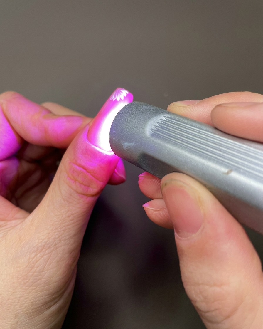 Ein Nailart-Werkzeug trägt einen kleinen Punkt klares Modelliergel auf die Nageloberfläche in der Nähe der gemalten Blumen auf.