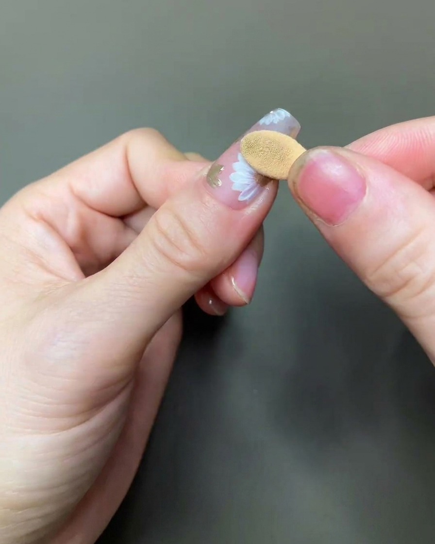 Nahaufnahme eines Schaumstoff-Applikators, der vorsichtig goldenes Chrom-Pigment auf die Mitte eines gemalten Gänseblümchen-Designs aufträgt.
