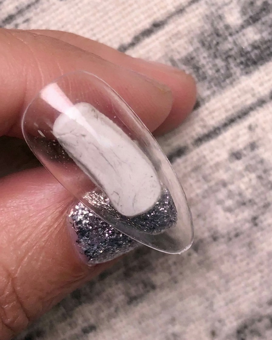 Ein Pinsel trägt klaren Transferkleber auf einen transparenten Nagel-Tip auf.