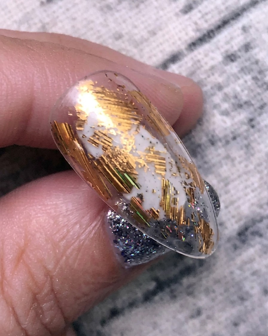 Anwendung von Gold-Transferfolie auf einer Nageloberfläche mit einem Silikonwerkzeug.