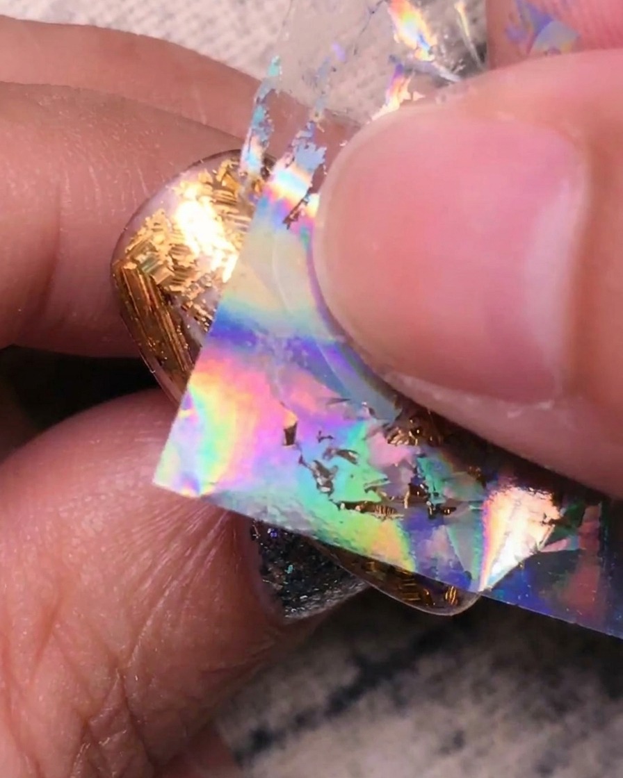 Andrücken von holografischer Silberfolie auf die verbleibenden klaren Bereiche des Nagels.